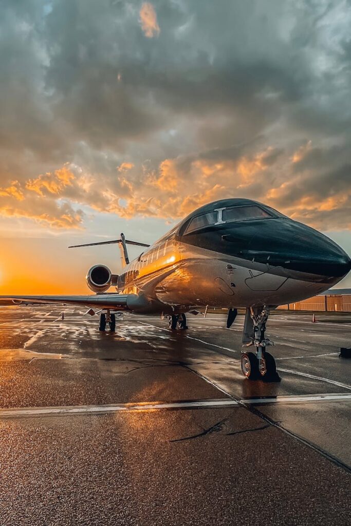 A sleek private jet parked on a wet tarmac during a colorful sunset at an airport.